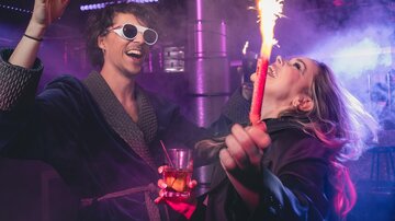 Eine fröhliche Partyszene mit zwei Menschen, die mit glühenden Funken spielen. Sie haben Spaß, während sie in einer lebendigen Umgebung feiern.