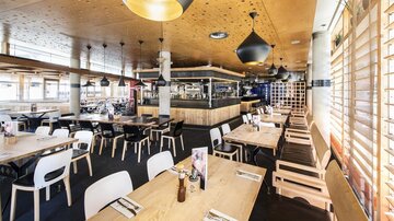 Ein modernes Restaurant mit hellem Holzinterieur und stilvollen Lampen. Die Tische sind ordentlich eingedeckt und bieten Platz für Gäste.